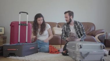 Adam dikkatsizce karısının bavuluna bir şeyler atıyor, seyahat öncesi bavul hazırlıyor, video çekiyor. 