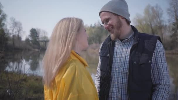 年轻貌美的一对夫妇在外面的河里散步 漂亮的金发女郎穿着黄色雨衣与一个留着胡子的男人调情 — 图库视频影像
