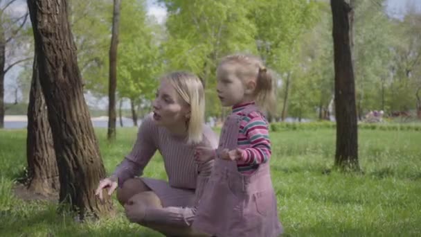 可爱的小女孩和她的母亲在公园里玩耍 用一个小指头指指着 那个女人向她的孩子解释世界是怎样的 无忧无虑的孩子与单亲在户外休息 积极健康的生活方式 与自然的联系 — 图库视频影像