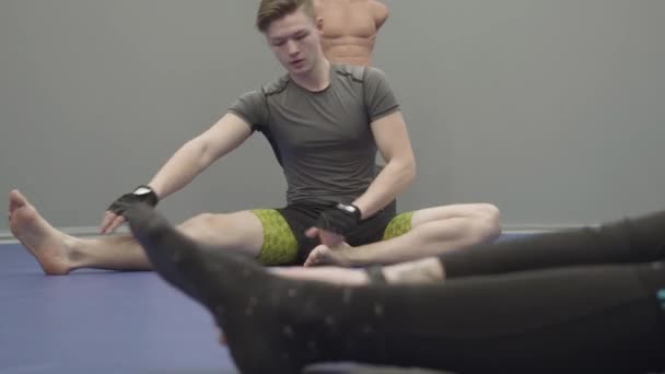 若いですブロンドハンサムな男座っている床とストレッチ彼の足でザジム — ストック動画