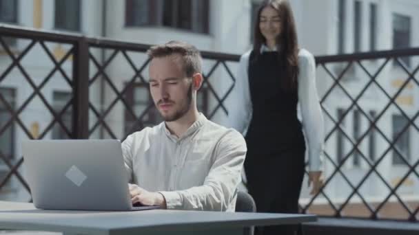 髭を生やした若い男がノートパソコンの前のテラスのテーブルに座って 屋外で働いていた きれいな女の子が来て 画面上で見て ビデオ — ストック動画
