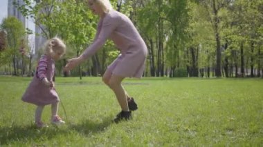 Genç anne dayanır, kusar ve bahar günü kızını doğada döndürür. Parkta oynayan kadın ve çocuk. Arkadaş canlısı mutlu aile kavramı.