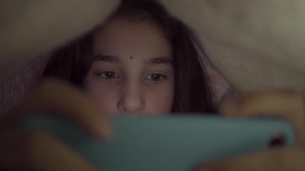 Schattig Tienermeisje Speelt Haar Mobiele Telefoon Liggend Onder Deken Van — Stockvideo
