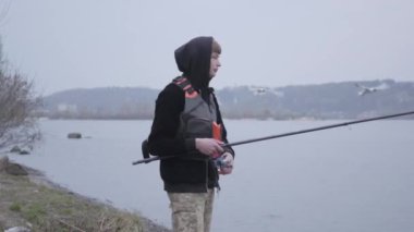 Sabahın erken saatlerinde kentin yakınlarındaki nehirde balık tutarken haki pantolonlu kendinden emin bir balıkçı.