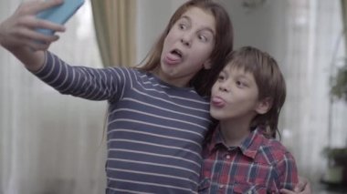 Ablası küçük erkek kardeşiyle selfie çekiyor. Yakın çekim. Çocuklar surat yapar, poz verir komik görünmeye çalışırlar. Tasasız çocukluk. Mutlu aile