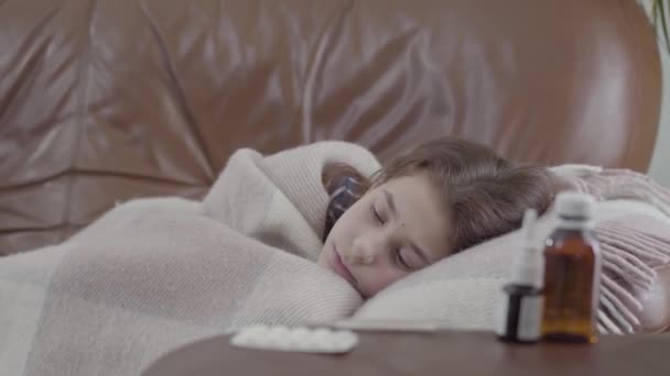 10代の病気の少女はソファの上に毛布で覆われて自宅に横たわって 彼女は寒いです 手前のテーブルの上にナサルスプレー シロップ 医療の概念 カメラが左へ — ストック動画