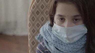 Yüzünde tıbbi maske olan üzgün hasta kız aşağıya bakıyor, video 