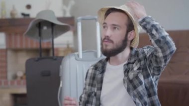 Şapka ve eşarp takan sakallı adam seyahat için büyük bavulların yanında, video