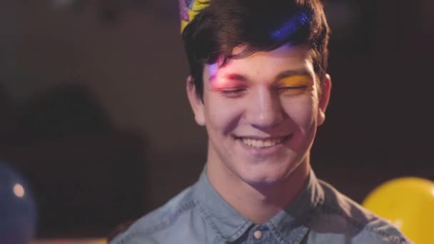 Retrato Joven Sonriente Con Sombrero Cumpleaños Mirando Cámara Luces Brillantes — Vídeo de stock