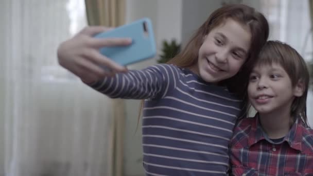 孩子们 姐姐和哥哥在家里用手机自拍 女孩们露出舌头 男孩们在笑 — 图库视频影像