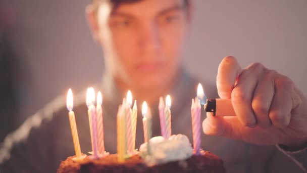 小さなケーキの前に座っている若い男がライターでろうそくを灯している 孤独な男は誕生日パーティーがある お祝いの概念 — ストック動画