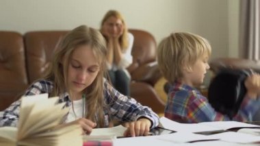 Anneleri arka planda otururken, küçük kız ve erkek çocukları ön planda ders çalışıyor. Kardeşi etrafta aylak aylak dolaşıp kafasına sırt çantası geçiriyormuş. Çocuklar ödevlerini yapıyor. 