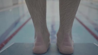 Profesyonel sporcu erkek yüzücü yüzme havuzuna kapalı havuzda başlangıç bloğundan atlıyor. Kapatın. Sağlıklı bir yaşam tarzı. Spor ve eğlence..