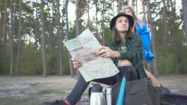 Hipster turist mutlu çift ekose gömlekli kahve içiyorlar ve seyahat sırasında ormanın arka planına bakıyorlar.