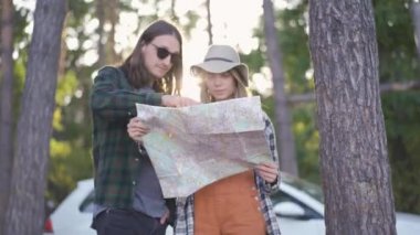 Şapkalı güzel bir kız ve güneş gözlüklü genç bir adam ormanda kalıp haritaya nasıl bakacağını seçmeye çalışıyor..