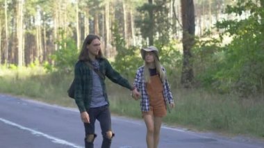 Milenyum turisti ekose gömlekli mutlu çift yol boyunca yürüyor ve ormanın arka planında birlikte seyahat ediyorlar.
