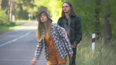 Hipster milenyum turisti ekoseli hippi gömlekli mutlu çift ormanda otostop çekerken araba yakalamak istiyor.
