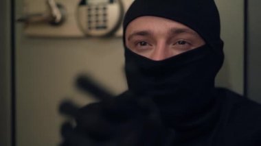 Siyah elbiseli, eldivenli ve ellerini ovuşturan kar maskeli genç beyaz bir hırsızın portresi. Kasadan bir şeyler çalan adam. Suç kavramı, suç, kanuna karşı suç