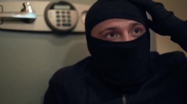 Siyah elbiseli ve kar maskeli genç hırsız kasaya bakıyor. Beyaz adam daireden bir şeyler çalıyordu. Suç kavramı, suç, kanuna karşı suç