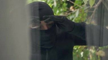 Siyah elbiseli ve kar maskeli hırsızın pencereden eve bakışını yakından çek. Yasalara karşı suç, suç, soygun kavramı