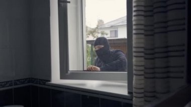 Siyah elbiseli ve kar maskeli hırsızın penceresinden eve girerken yakın plan fotoğrafı. Yasalara karşı suç, suç, soygun, hırsızlık kavramı