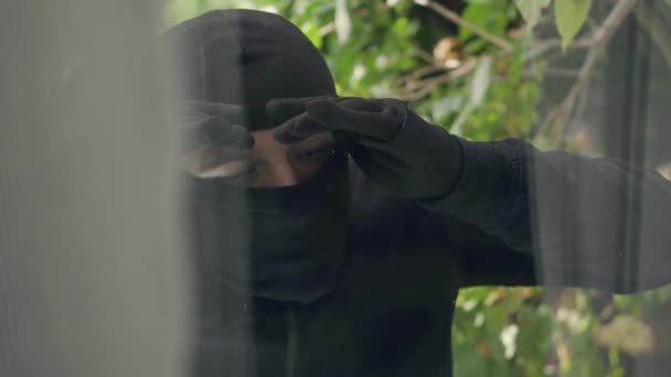 那个穿黑色衣服 头戴巴拉克拉瓦的小偷的特写镜头 透过窗户向屋内看去 违反法律 抢劫的概念 — 图库视频影像