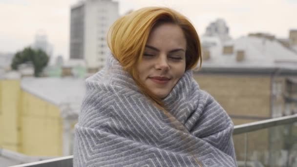 毛布に覆われた赤い髪をした白人女性の肖像画 少女はカメラがバルコニーに立っているのを見た 秋のレジャー 屋外で休む — ストック動画