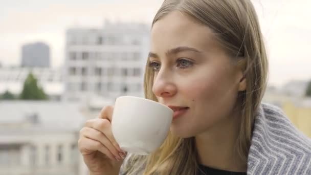 若い白人女性が毛布でお茶やコーヒーを飲んでいた 少女はバルコニーに立って飲み物を楽しんでいる 秋のレジャー屋外 — ストック動画