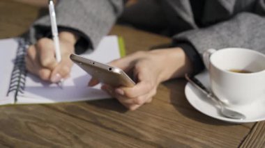 Kafedeki masada otururken cep telefonu tutan genç beyaz bir kadının yakın çekimi. Defterine yazan kız. Serbest çalışan biri. Sonbahar tatilleri kapalı alanlarda 
