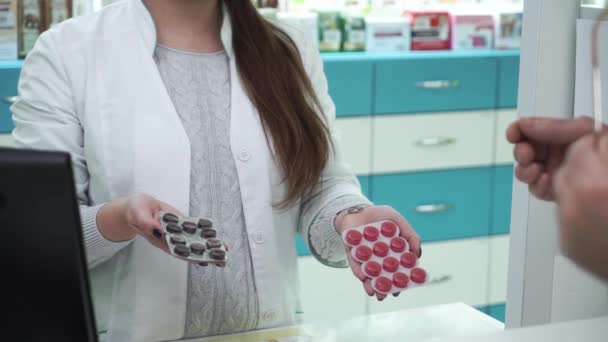 Onherkenbare vrouwelijke apotheker voorstellen van twee varianten van medicijnen aan de klant. Mannelijke koper kiezen tussen zwarte en rode pillen voor de behandeling. Gezondheidszorg en traditionele geneeskunde. — Stockvideo