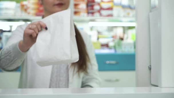 Ο χαμογελαστός φαρμακοποιός δίνει τη λευκή χάρτινη σακούλα με φάρμακα στον αρσενικό πελάτη. Διαδικασία αγοράς στο φαρμακείο. Υγειονομική και παραδοσιακή ιατρική έννοια. — Αρχείο Βίντεο