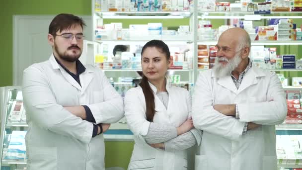 Tres farmacéuticos caucásicos de diferentes edades mirándose y sonriendo a la cámara. Empleados altamente profesionales que permanecen en su lugar de trabajo. Personas con túnicas blancas destinadas a rescatar vidas . — Vídeo de stock