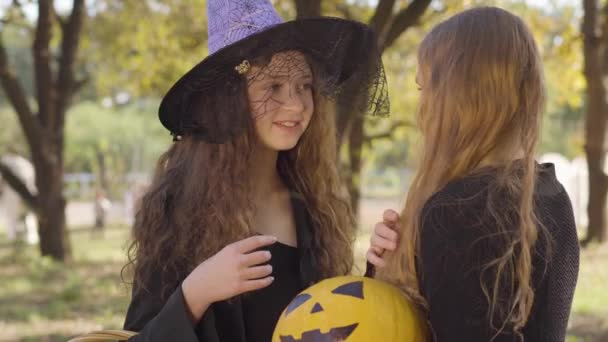 可爱的高加索红头发女孩穿着巫婆的服装和她的金发朋友说话 两位小朋友讨论庆祝圣夜的事 — 图库视频影像