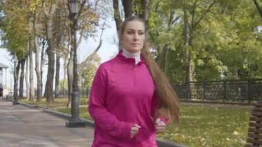 Pembe spor giysili beyaz bir kadın göğüs ağrısı yüzünden koşuda duruyor. Bayan koşucu sonbahar parkında sabah antrenmanında kendini kötü hissediyor. Spor ve sağlık konsepti.