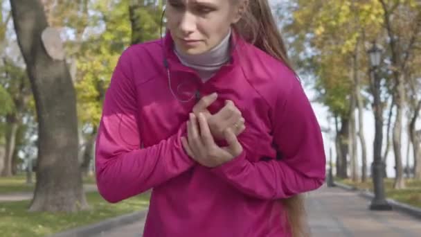 一位漂亮的白种人女子穿着粉色运动服 胸部疼痛的特写 在秋季公园的晨练中 女赛跑选手感觉很糟糕 体育和保健概念 — 图库视频影像
