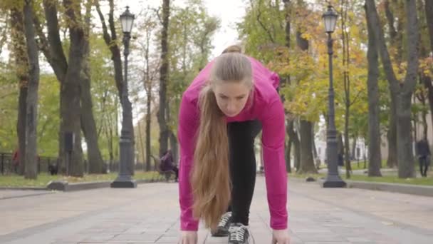 Впевнена, що молода кавказька жінка дивиться вгору і починає бігати. Приваблива жіноча підготовка бігуна вранці в осінньому парку. Зомби камери. — стокове відео