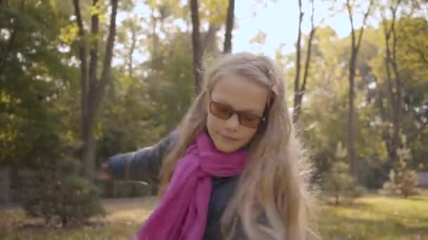 秋の公園や森の中のショットから出てくる長いブロンドの巻き毛を持つ陽気な白人の10代の少女の肖像画 女子高生は屋外で楽しい時間を過ごしています — ストック動画