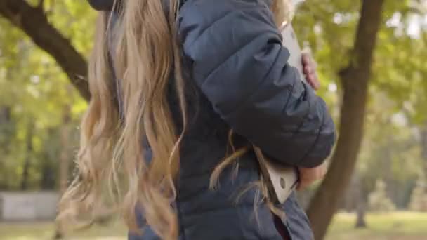 一个年轻的白人女性手牵着笔记本电脑的特写镜头 年轻的女学生带着她的装置在秋天的公园或森林里散步 — 图库视频影像