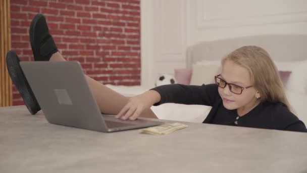 快乐的白人少女坐在她的房间里 拿着笔记本电脑 有自信的年轻女学生 腿放在桌子上享受周末 — 图库视频影像