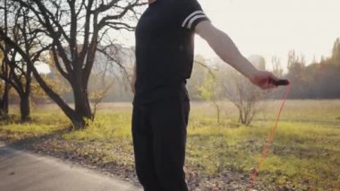 Günbatımında sonbahar parkında siyah spor kıyafetleri içinde ip atlayan beyaz bir çocuk. Yarışmalardan önce açık havada güçlü bir sporcu antrenmanı. Sağlıklı yaşam tarzı spor konsepti.