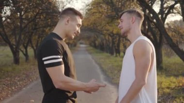 Sonbahar parkında gün batımında kaslarıyla övünen iki beyaz sporcu. Genç vücut geliştiriciler güneşli bir günü dışarıda geçiriyorlar. Sağlıklı yaşam tarzı kavramı