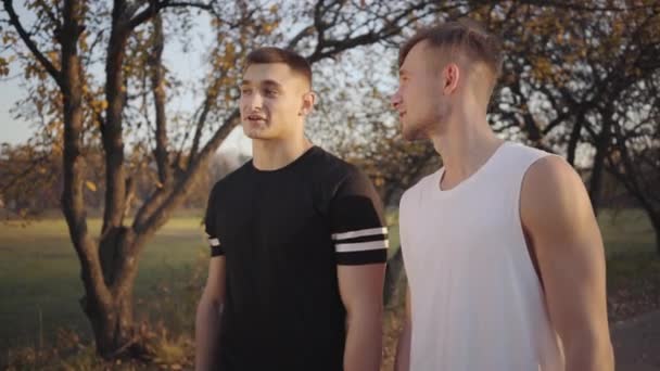 Zwei Kräftige Kaukasische Jungs Sportkleidung Stehen Herbstpark Sonnenlicht Und Unterhalten — Stockvideo