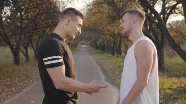 两名积极的白人运动员站在秋天公园的落日下 夸耀他们的肌肉 年轻的健美运动员在户外度过阳光灿烂的一天 健康生活方式概念 — 图库视频影像