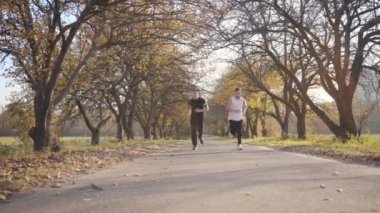 Sonbahar parkında koşan iki beyaz çocuk. Yetişkin sporcular yürekleri sızladığı için dururlar. Sağlıklı yaşam tarzı kavramı