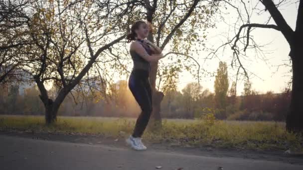 日没の秋の公園で若い白人の少女のロープワークアウトをジャンプします 屋外で黒のスポーツウェアの訓練の女性 健康的なライフスタイル スポーツコンセプト — ストック動画
