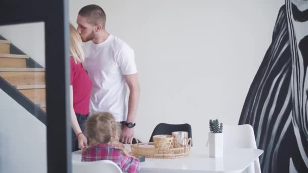 Gelukkige jongeman met tatoeages op handen zoenen vrouw en dochter thuis. Portret van een vrolijke blanke familie die samen in het weekend doorbrengt. Lifestyle, vrije tijd, eenheid, liefde. — Stockvideo