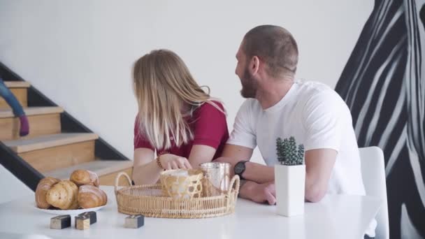 Vrolijk jong stel dat hun mooie dochtertje van houten trappen ziet lopen. Portret van een blanke man en vrouw die 's ochtends samen met het kind binnen zijn. Liefde, vreugde, levensstijl. — Stockvideo