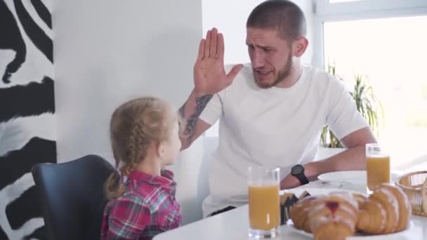 Grappige vrolijke getatoeëerde man speelt high five met kleine blonde dochter thuis. Portret van een blije vader die een weekend doorbrengt met een kind binnen. Vrije tijd, verbondenheid, familie, levensstijl. — Stockvideo