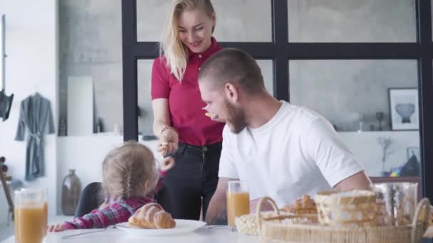 Leende ung kvinna ger välsmakande näringsvitaminer till söt dotter och lycklig make. Porträtt av uppmärksam kaukasisk mor och hustru som tar hand om familjen. Hälsa, enhet, livsstil. — Stockvideo