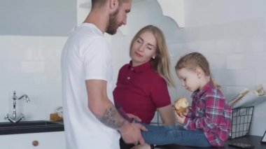 Genç bir anne ve baba mutfakta neşeli tatlı bir kızla oynuyorlar. Kafkas erkek ve kadın portresi hafta sonları güzel kızıyla kruvasan çiğniyor. Boş zaman, rahatlama, yaşam tarzı..